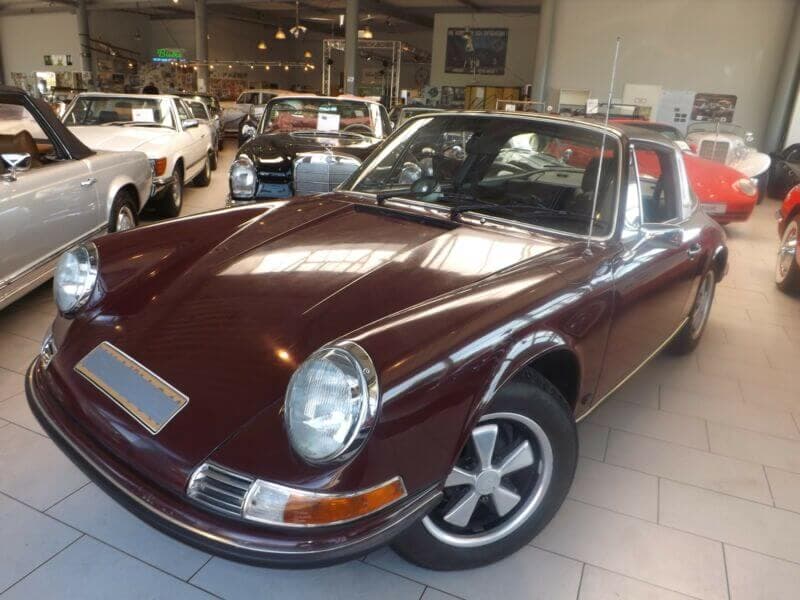 Dieses Foto zeigt den Porsche Targa, einen Oldtimer aus dem Jahr 1970, der aktuell bei My Next Classic zum Verkauf angeboten wird. Es handelt sich um ein sehr seltenes Fahrzeug mit Erstlack in burgunderrot und mit einem prominentem Vorbesitzer - dem ehemaligen Schalke 04 Fußballspieler Reinhard „Stan“ Libuda.